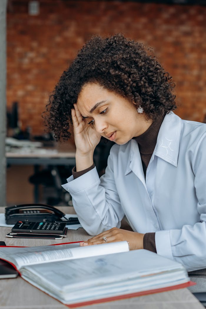 pexels-photo-8297234 Exhausted woman in office with paperwork, displaying signs of stress.